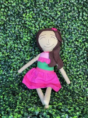 A doll is laying on the ground with green leaves.