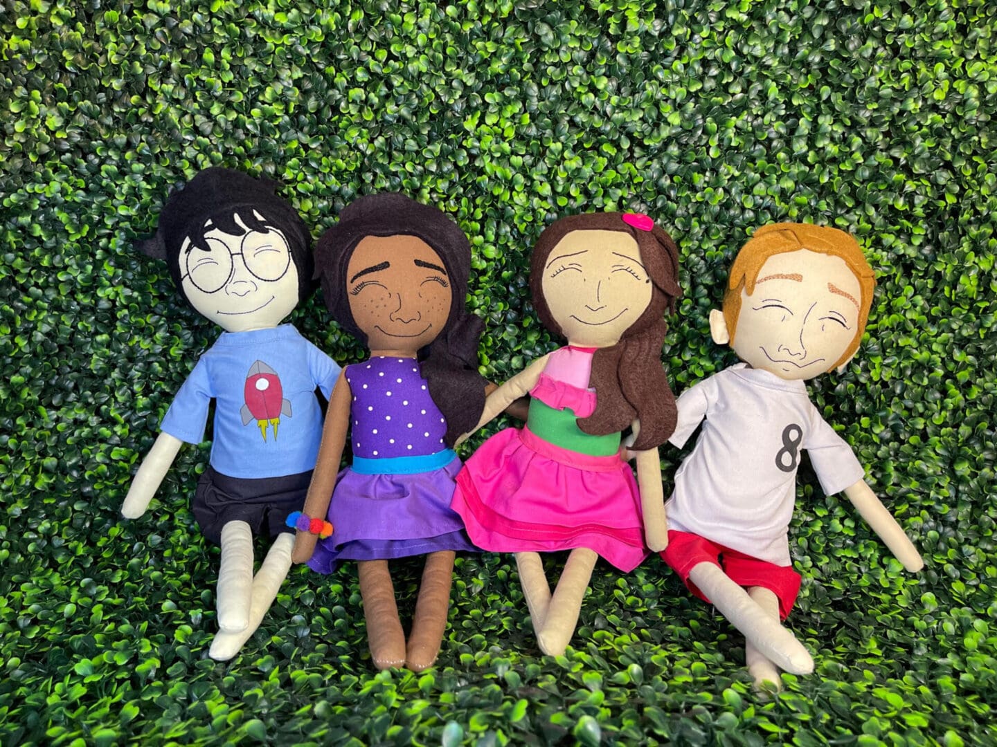 A group of four dolls laying on top of green grass.